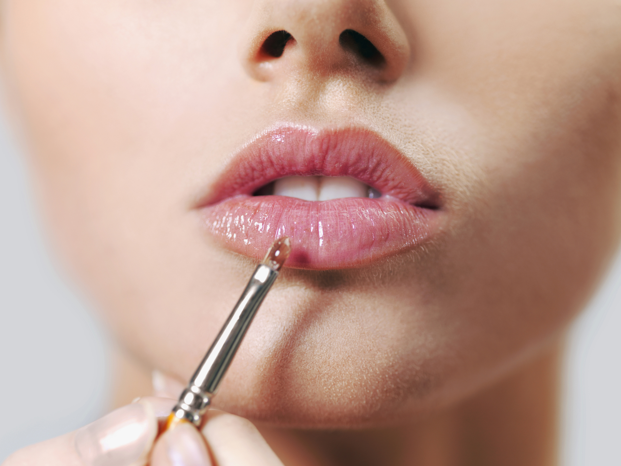 A woman applying lip gloss with a make-up brush, close-up of lips